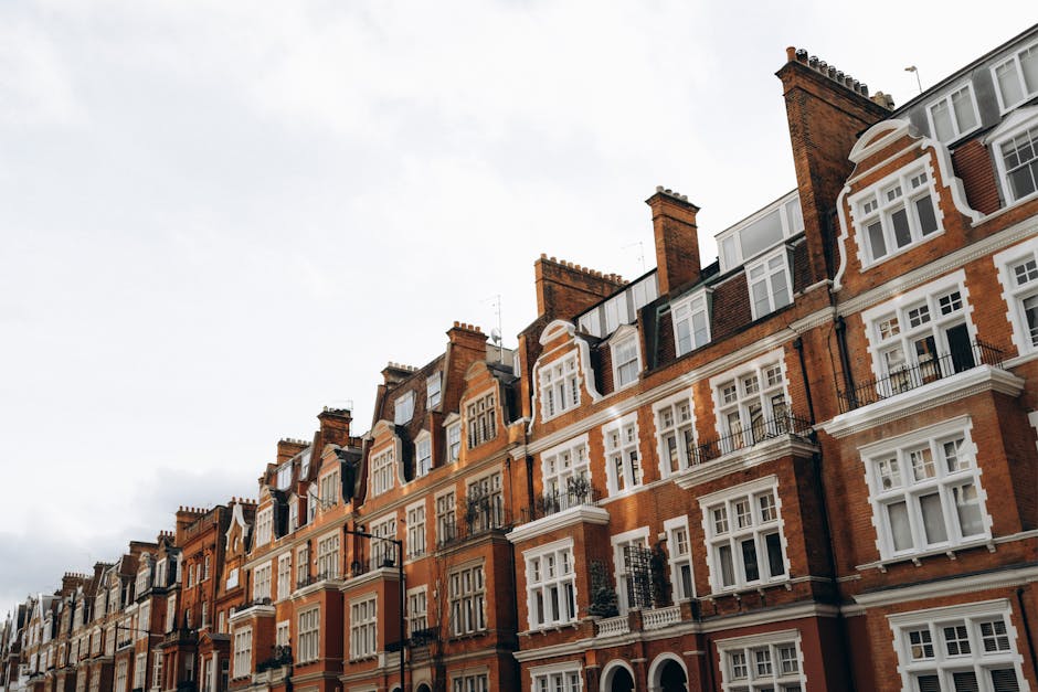 A brick residential building with a dark red and brown textured facade featuring three white-framed windows on the upper floor, one of which is open with partially visible blinds inside, and three arc
