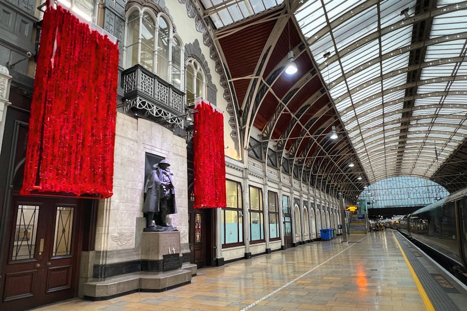 Inside a spacious train station with an arched, glass-paneled roof supported by intricate metalwork, a modern high-speed train with a sleek black and yellow exterior is positioned on the platform. The